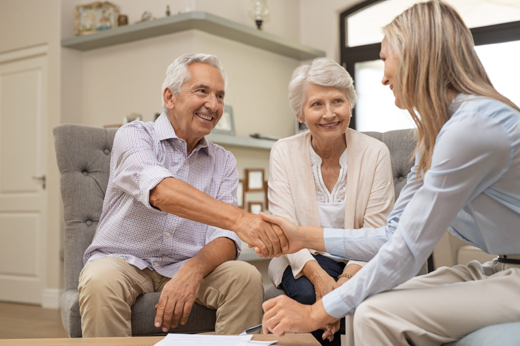 Happy senior couple sealing with handshake a contract for the retirement. Smiling satisfied retired man making sale purchase deal concluding with a handshake. Elderly man and woman smiling while agree with financial advisor.