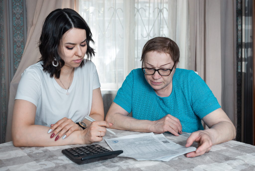 Young woman and an old lady are checking bills for payment, checking domestic finances, managing middle-aged families, budget planning, expenses, an elderly woman reading bank loan documents at home