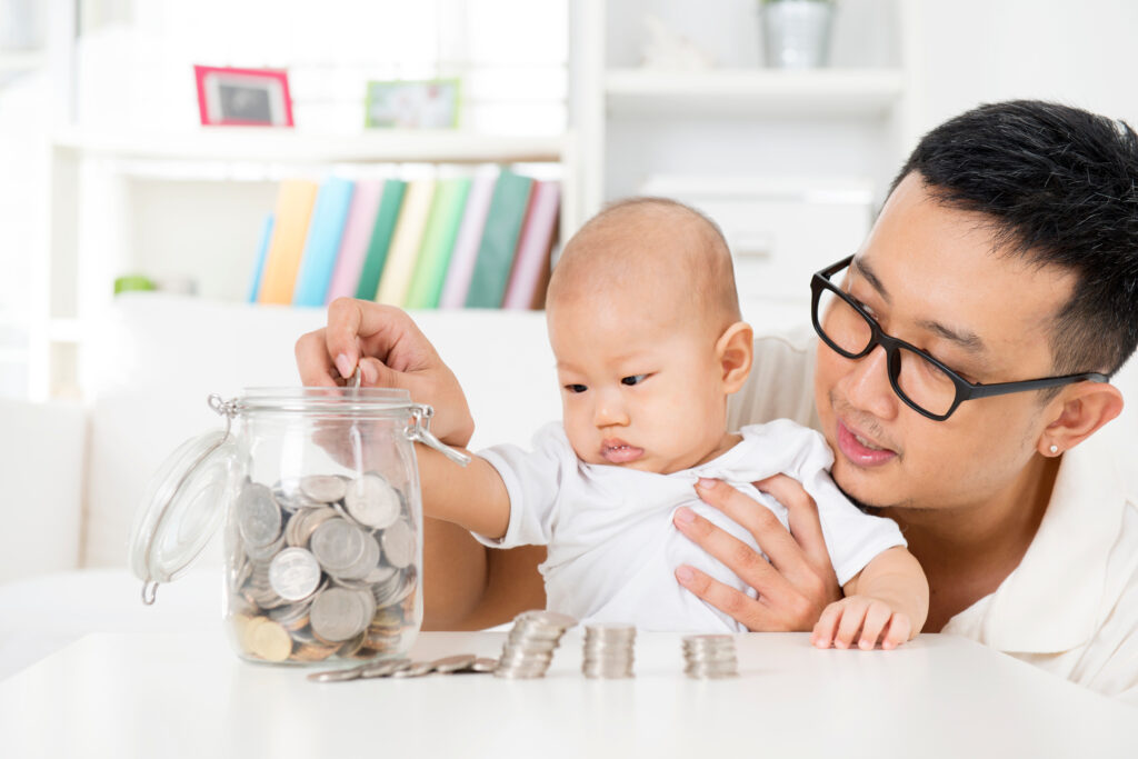Asian family lifestyle at home. Father and baby putting coins into money jar, financial planning concept.