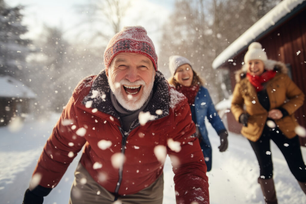 Portrait of happy senior man in winter during snow having fun with family outdoors playing snowballs fight. Active healthy lifestyle in retirement.