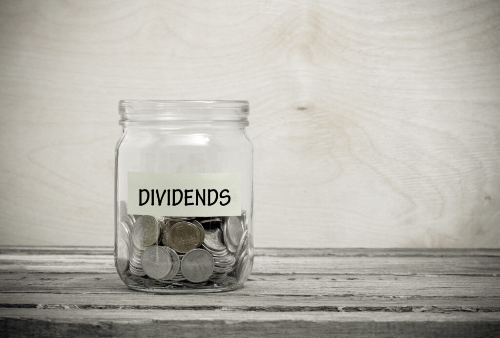 Label on a glass jar with the inscription - dividends. Glass jar with coins. Financial concept on wooden background